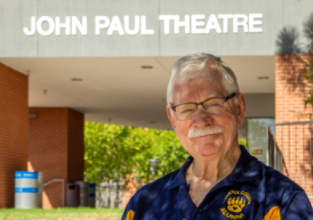 Marty Manning stands in his Phoenix College alumni shirt in front of John Paul Theatre