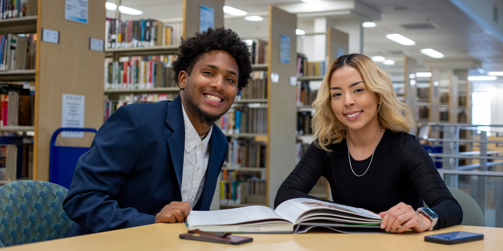 two students looking up from studying a book in the library