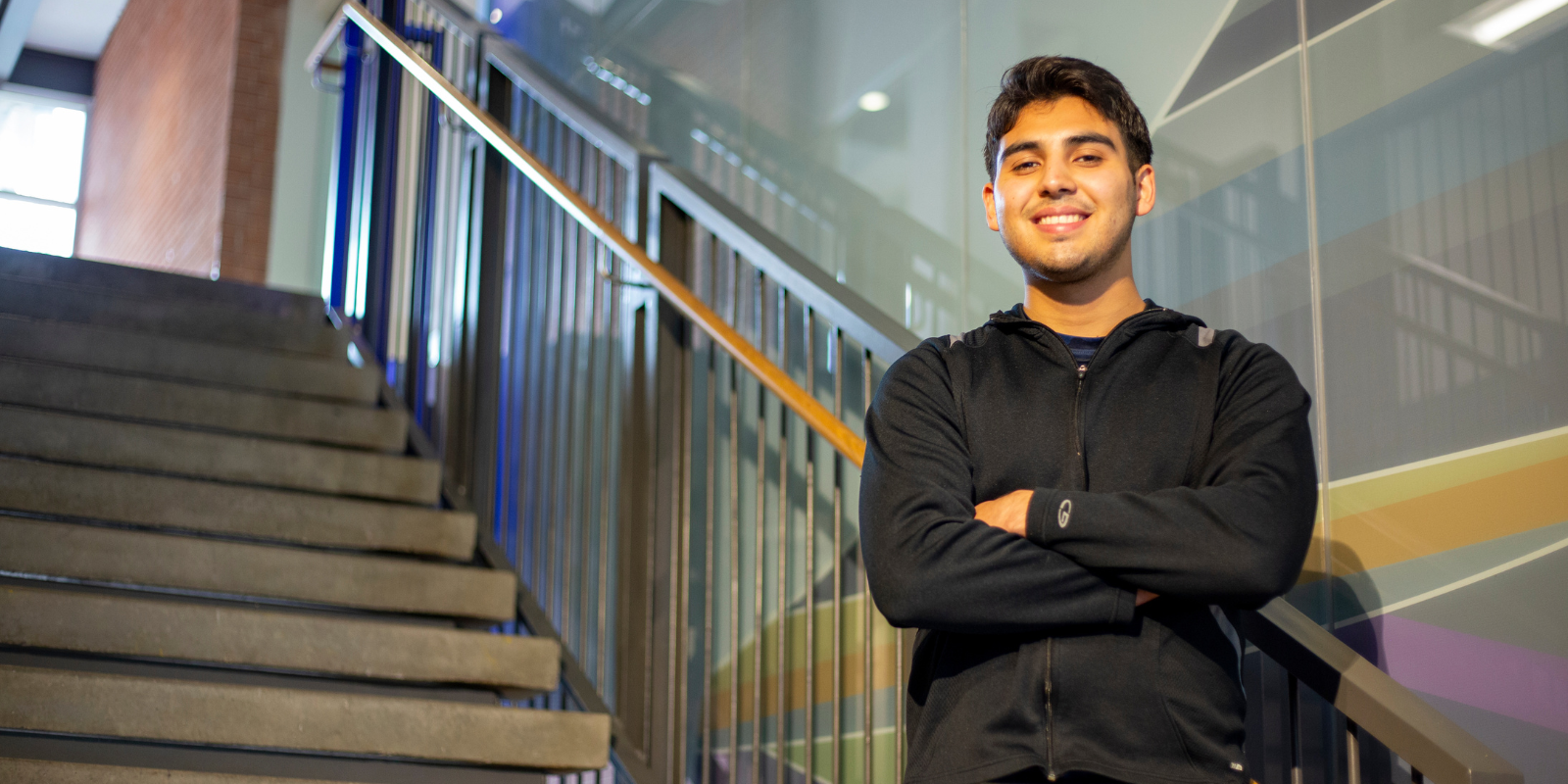 Male student in black standing on steps in the Physical Sciences building with arms crossed