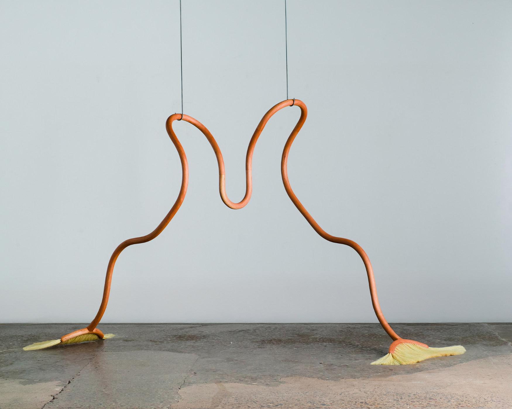 Two wooden brooms bent and melded together
