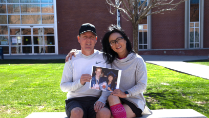 Phoenix College Alumni Jae Staats and Nancy Chong sit on a bench outside Bullpitt Auditorium, with the Phoenix College library in the background, holding a picture of themselves at their 1993 PC graduation