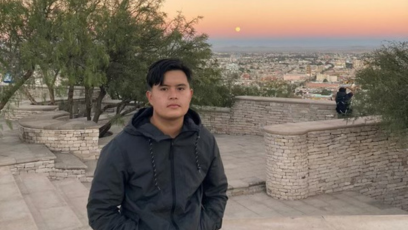 Phoenix College alumnus Luis Herrera sits on a stone wall with a sunset as a backdrop