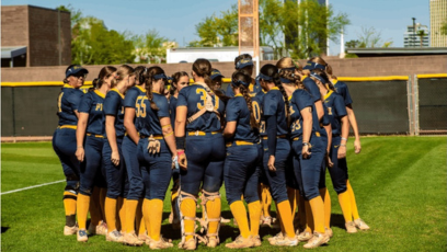 PC Softball players stand in a huddle on the softball field. 