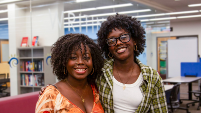 Sister Shadé and Sy'nai Ajayi stand side by side, smiling, in Phoenix College's Learning Commons where they both work while attending school for Medical Assisting and Elementary Education respectively
