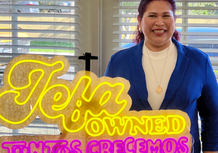 Imelda Hartley of Imelda's Happy Tamales standing with the Junto Crecemos, Jefa-owned neon sign awarded by Pepsico