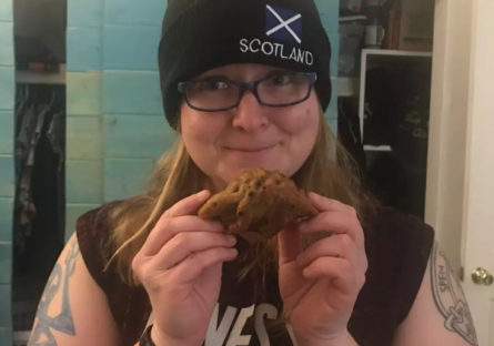 Phoenix College faculty Allison Hawn, wearing a Scotland hat, holding dinosaur banana bread from a student.