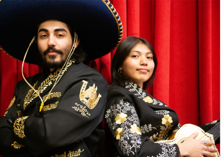 Two Phoenix College mariachi performers stand back to back in their trajes with a red backdrop