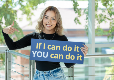 Jasmin in the Dalby Building holding up a sign that states, "If I can do it YOU can do it"