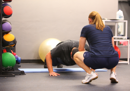 A man performs push ups with a female fitness coach in Phoenix College's Fitness Center