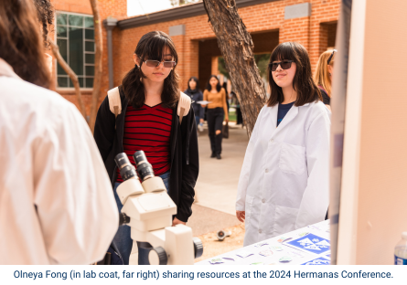 Sixteen-year-old Olneya Fong, Phoenix College graduate and high school senior, in a white lab coat at the Hermanas conference offering participants an opportunity to look into a microscope. 