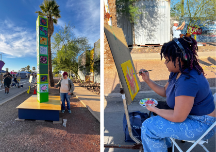 A Phoenix College student stands next to the "Block Party" installation, while another student completes a painting at the festival to be installed on one side of a block. 