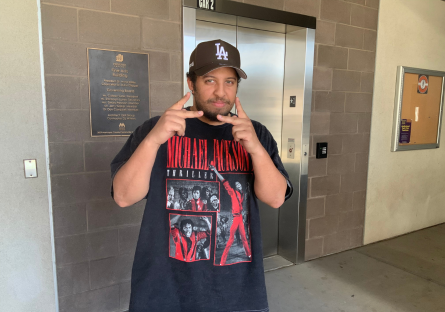 PC student and music producer Devon Ellison wears a black and red Michael Jackson thriller t-shirt and a black LA baseball cap and holds the index and middle fingers of both hands to frame his lower face