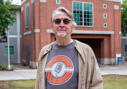 PC student Joe Drzewiecki stands on campus wearing a gray and orange PC Music Industry Studies t-shirt