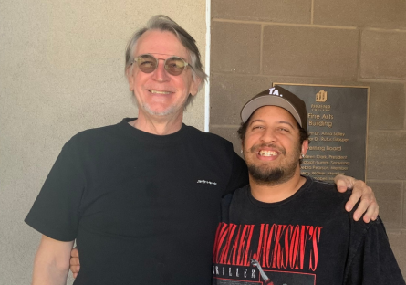 PC students and audio producers Joe Drzewiecki and Devon Ellison stand next to each other in black t-shirts, smiling, with Joe's left hand on Devon's left shoulder 