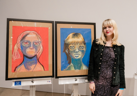 Phoenix College artist Ellie Gratrix stands to the write of her two pastel drawings "Blaze" and "Melancholy" which won her Vanguard Award in 2D