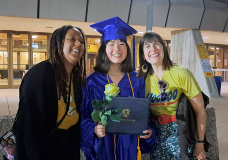Olina fond is wearing her graduation cap and gown and holding flowers standing between two of her teachers from PCPA
