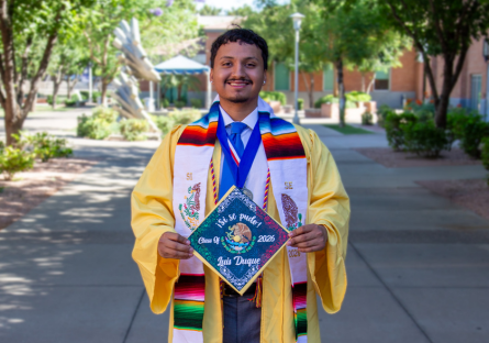 Luis Duque, graduate of Phoenix College with his Bachelor's Degree in Public Safety Administration holds his decorated graduation cap in front of him while standing on Phoenix College campus