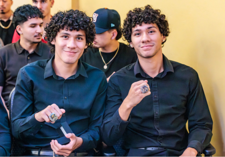 Two Men's soccer players sit in Bulpitt Auditorium admiring their newly presented champtionship rings