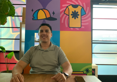 Cesar smiling behind a table with his graphic wall behind him
