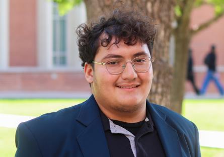 a young man poses for a picture in front of a library and tree