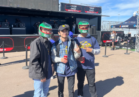 Rocket League players standing at Phoenix Raceway during NASCAR event, two wearing helmets