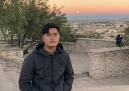 Phoenix College alumnus Luis Herrera sits on a stone wall with a sunset as a backdrop
