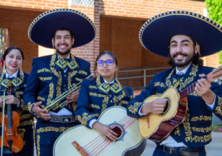 Four Phoenix College Mariachi Ensemble members stand on campus in their traditional trajes and their instruments