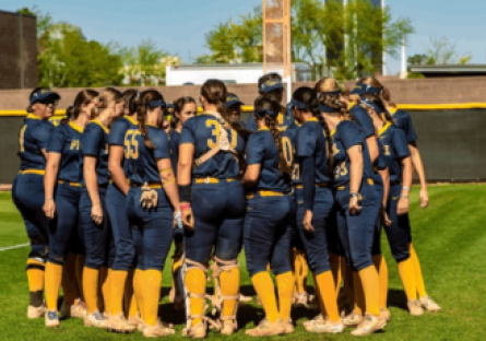 PC Softball players stand in a huddle on the softball field. 