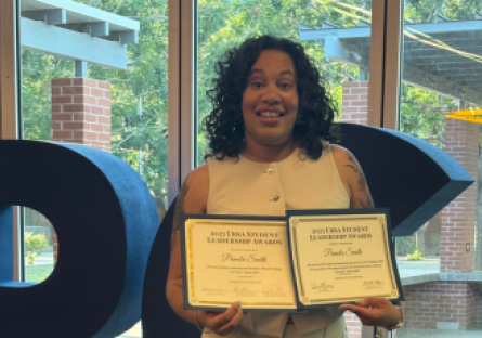 PC student Pamela Smith stands in the Student Union holding up two awards for her leadership