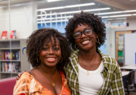 Sister Shadé and Sy'nai Ajayi stand side by side, smiling, in Phoenix College's Learning Commons where they both work while attending school for Medical Assisting and Elementary Education respectively
