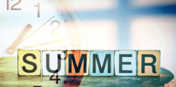 Half an analog clock and the block letters spelling summer on a table