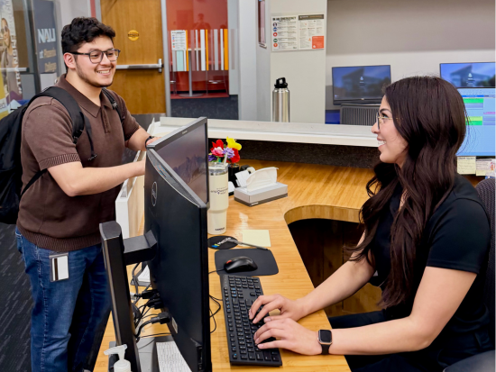 Woman sitting at checkin desk with hands on keyboard smiling and talking with student with backpack on alternate side of desk